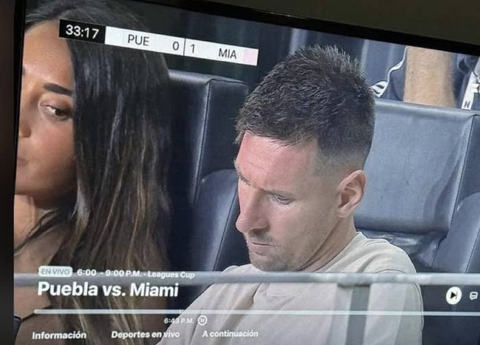 Lionel Messi and a woman are on screen during the Puebla vs. Miami Leagues Cup match. Messi appears focused, while the woman looks away