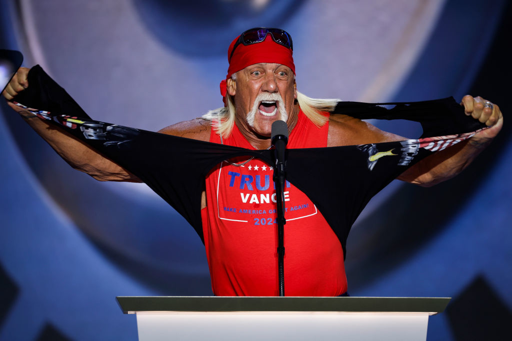 Hulk Hogan on stage wearing a bandana and sunglasses, tearing a shirt while speaking at a podium. Shirt has "Trump for Vance 2024" text