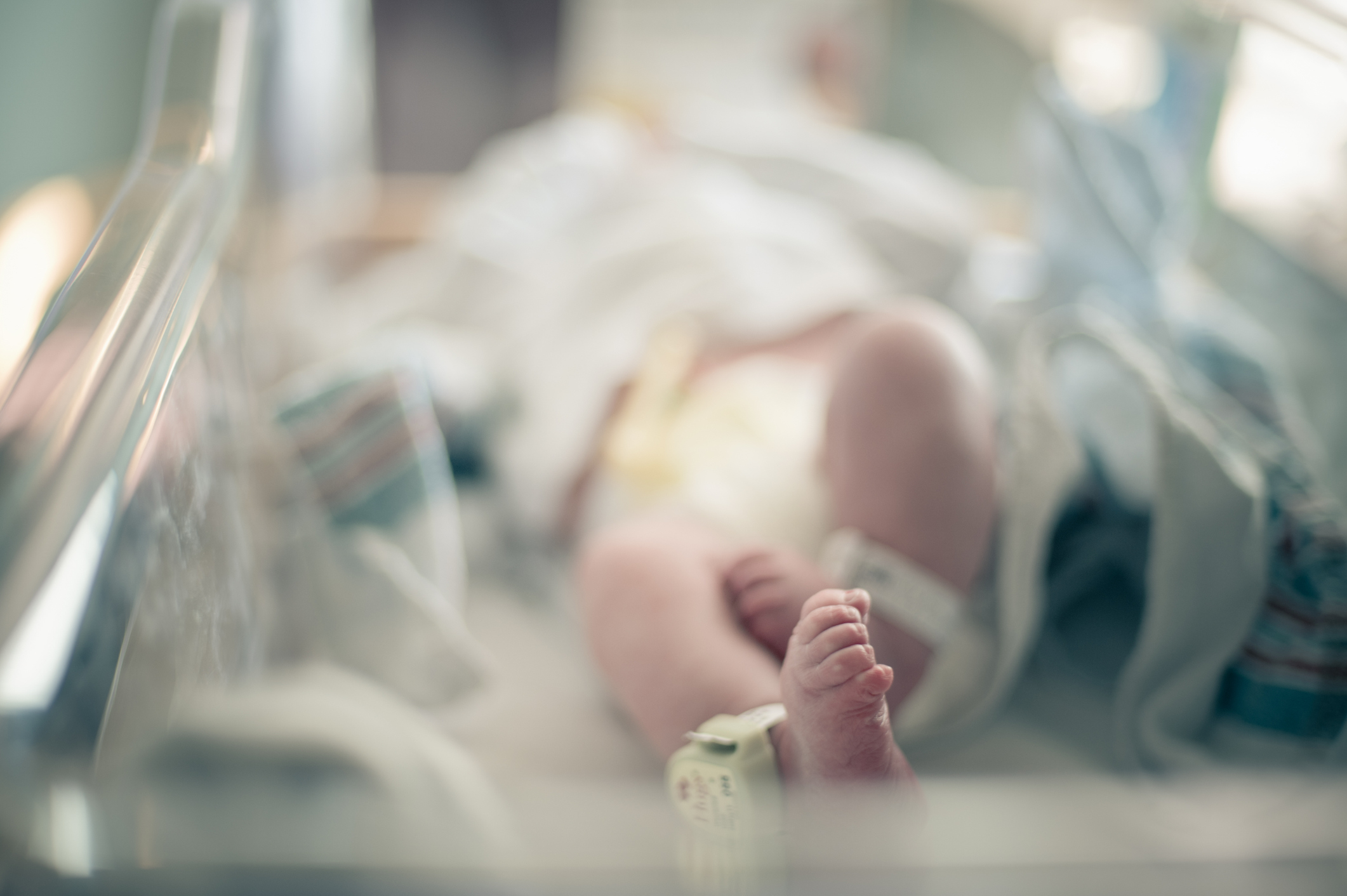 A newborn baby lies in a hospital crib, wrapped in blankets, with a name tag on their ankle, in an unidentified hospital setting