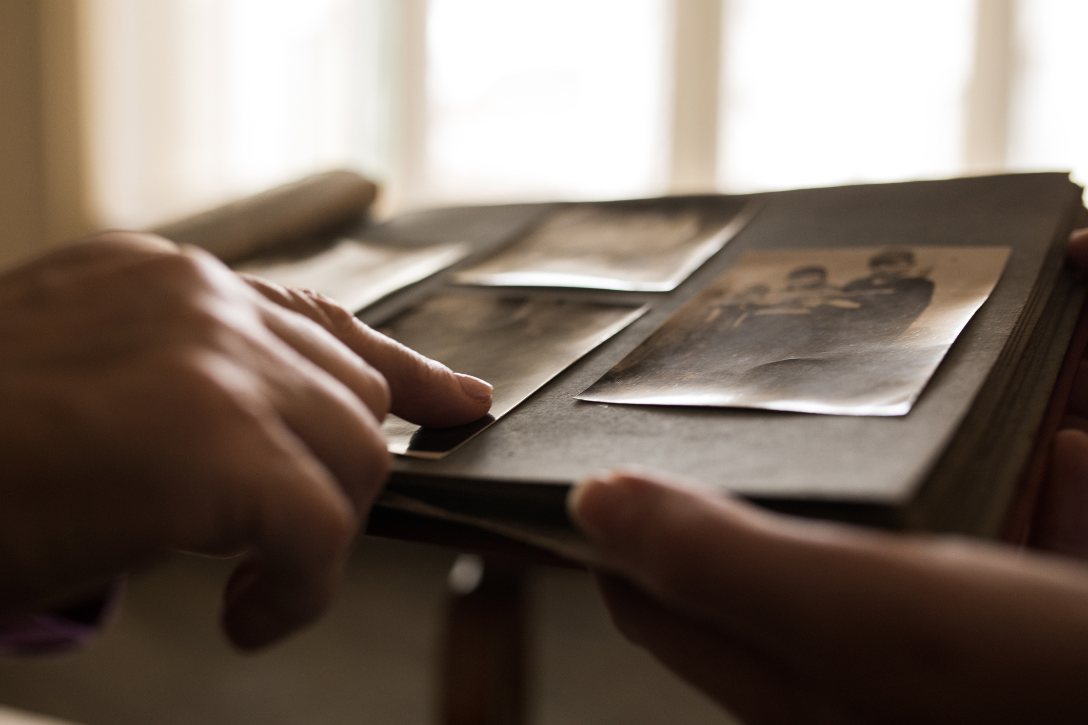 Hands flipping through an old photo album containing black and white photos of unidentified people