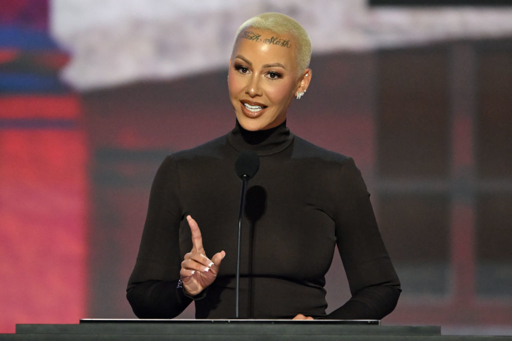 Amber Rose speaks at a podium, wearing a fitted turtleneck top, with short blonde hair