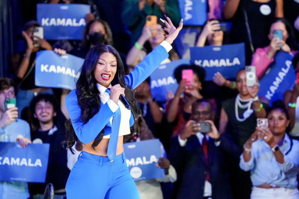 Megan Thee Stallion performs on stage in a suit in front of a crowd holding "Kamala" signs