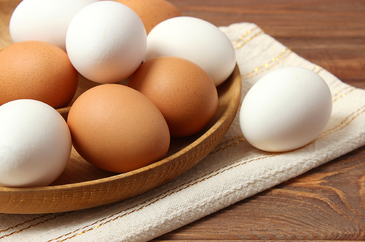 木製の皿に白と茶色の卵が盛られています。背景には布製のランチョンマットが見えます。