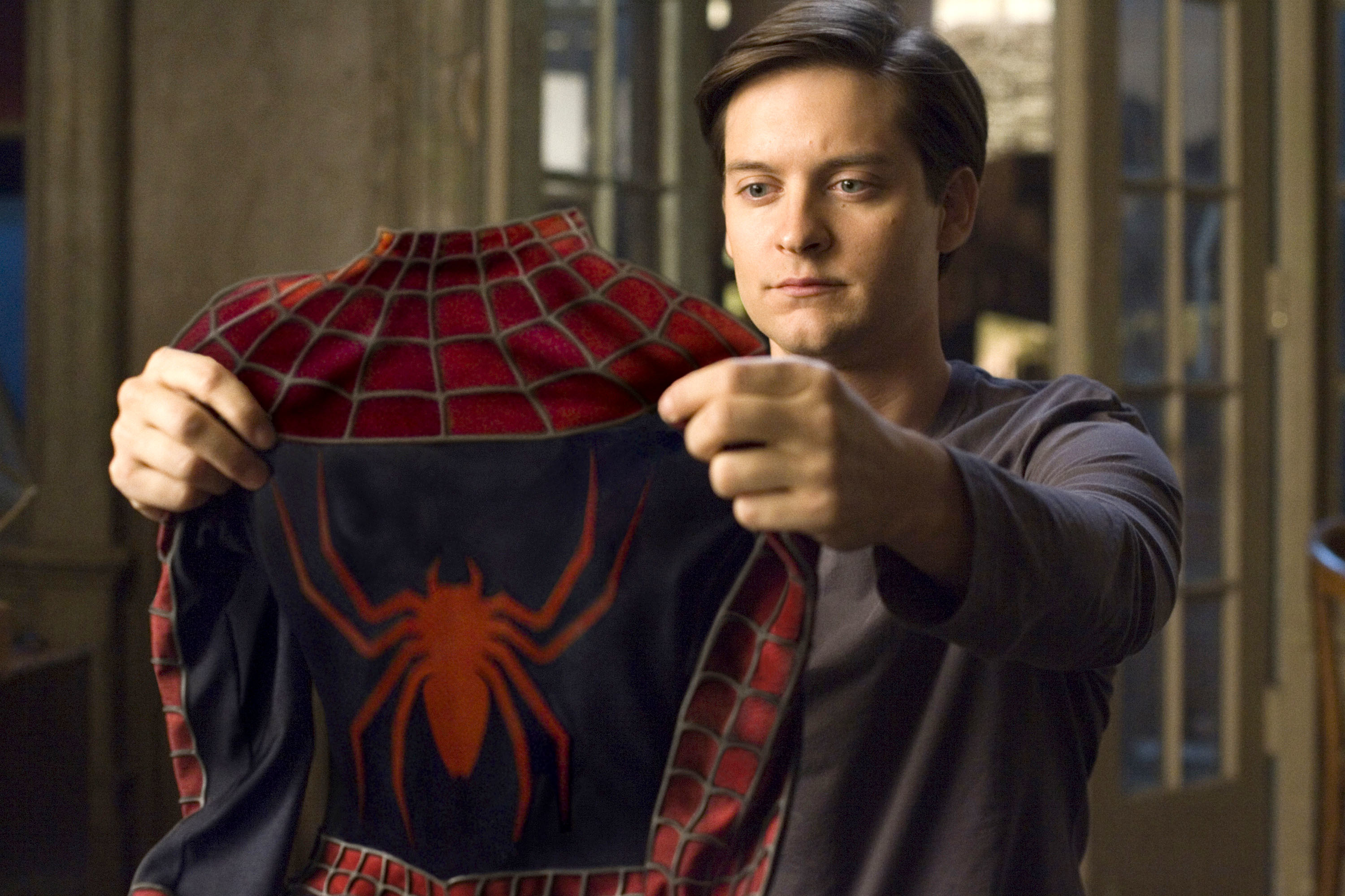 Tobey Maguire holds up a Spider-Man costume, examining it closely
