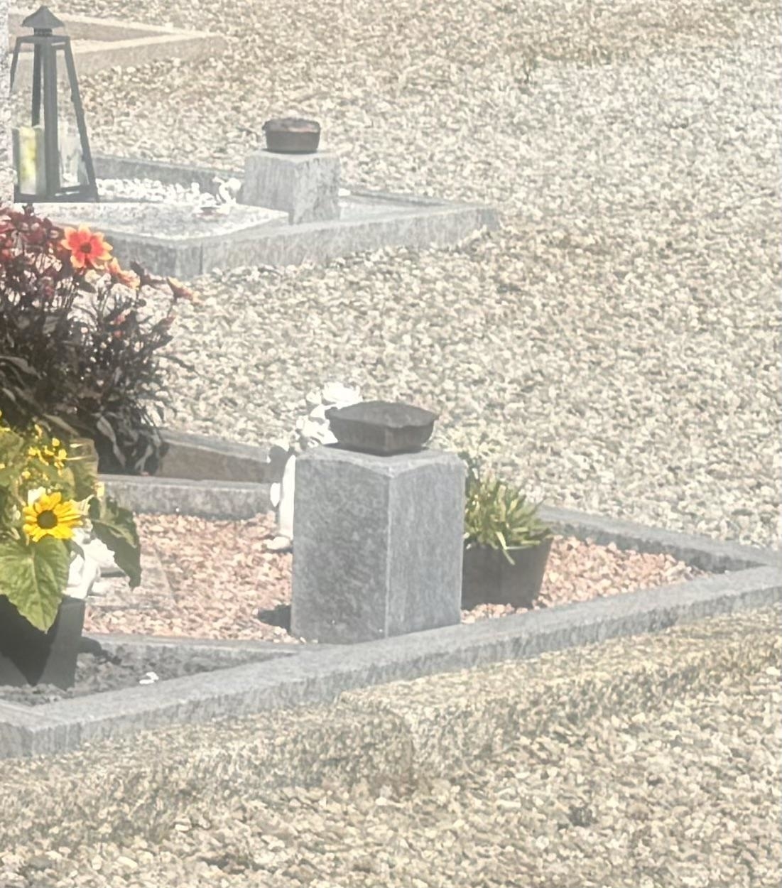 A grave site with flower arrangements and a lantern placed on and around the stone markers. The area is covered in gravel