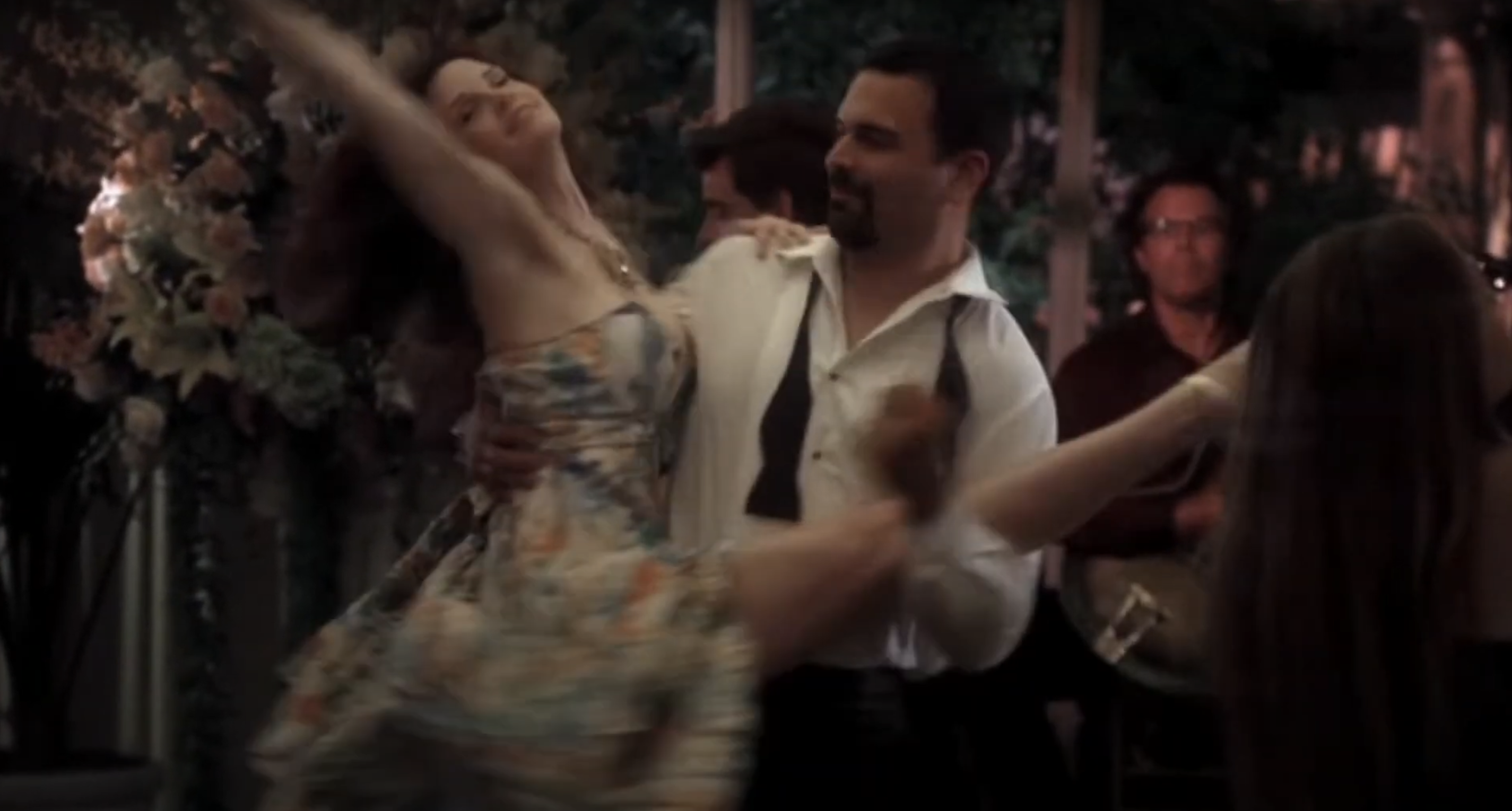 Marisa Tomei dances wearing a floral dress, lifted in the air by a man in a white shirt with a black suspenders. A band plays in the background