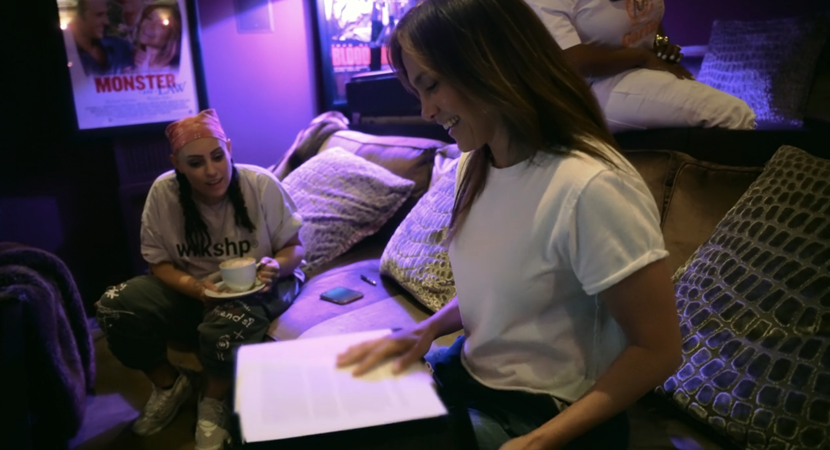 Two people in a cozy living space; one is holding a document and smiling, the other is sitting with a cup of tea