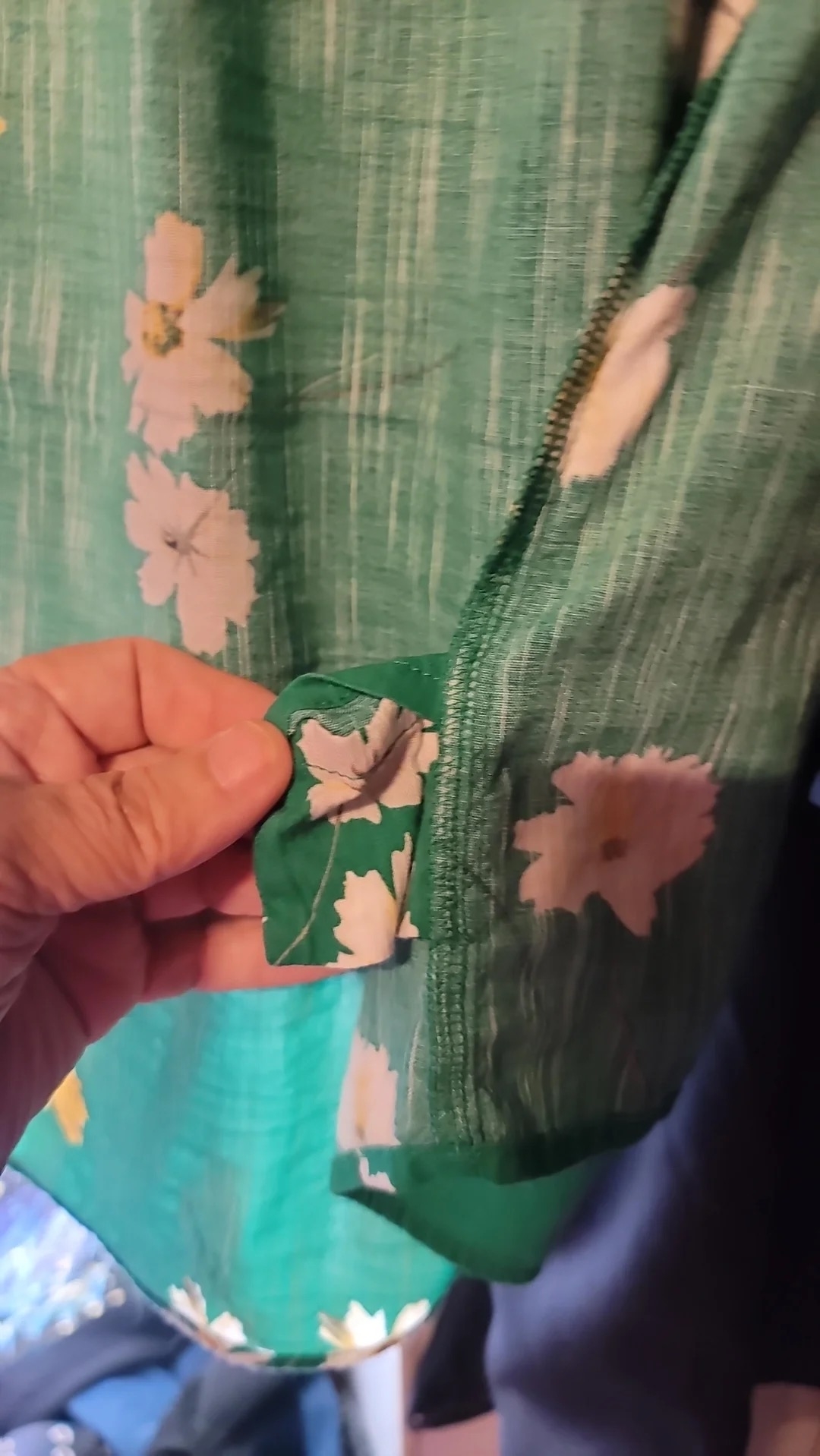 A person holds a green fabric with white flowers, showing a seam with a tiny pocket inside a mismatched floral pattern piece