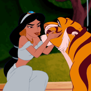Jasmine from Disney's Aladdin is feeding Rajah the tiger. Jasmine wears a two-piece outfit with gold accessories