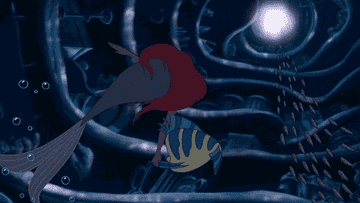 Ariel swims underwater with Flounder in a scene from The Little Mermaid, surrounded by sunken ship parts