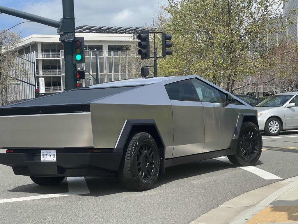 Futuristic, angular Tesla Cybertruck spotted driving through an intersection in an urban setting