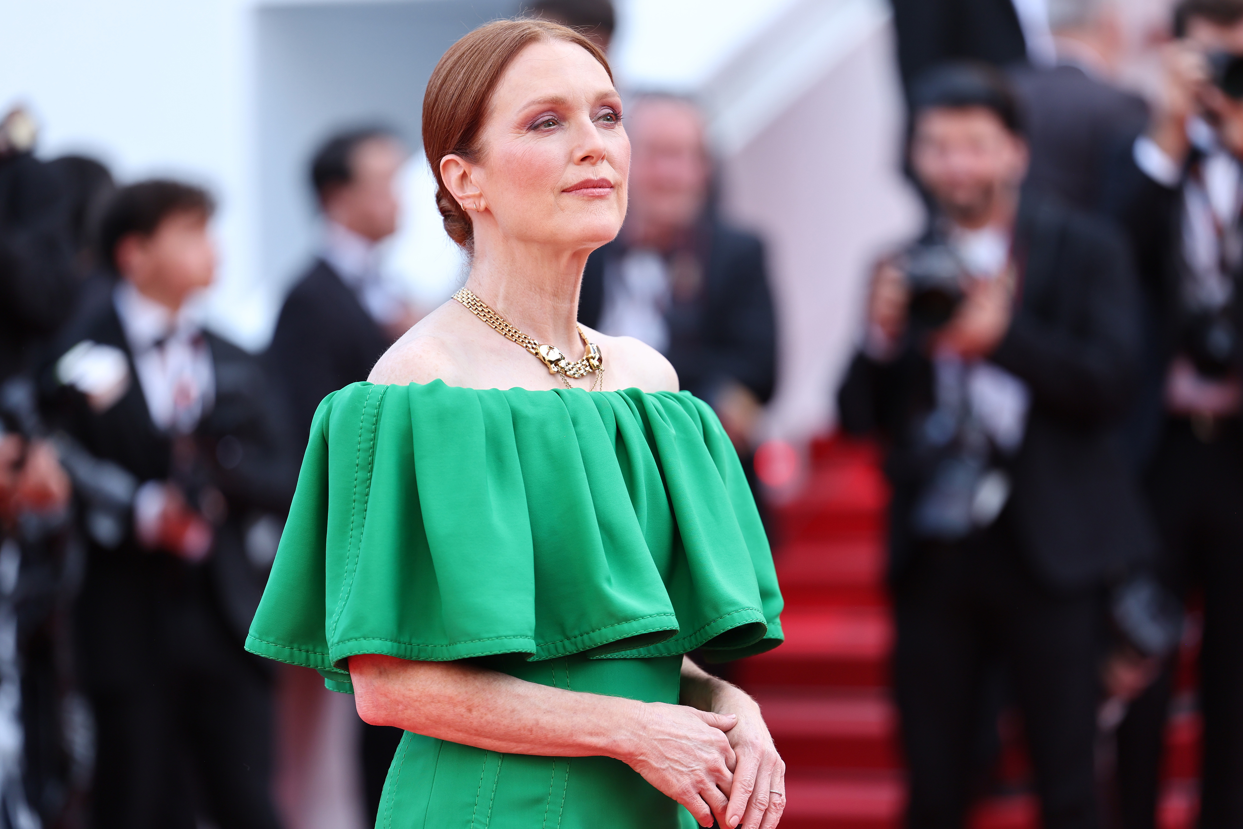 Julianne Moore on a red carpet, wearing an off-the-shoulder, ruffled green dress with a gold necklace