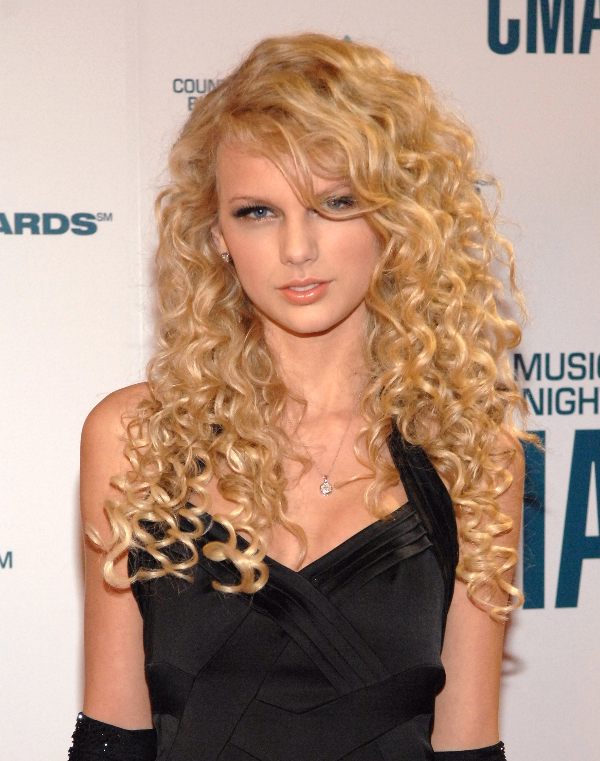 Taylor Swift on the red carpet in a black dress with spaghetti straps, her curly hair cascading over her shoulders