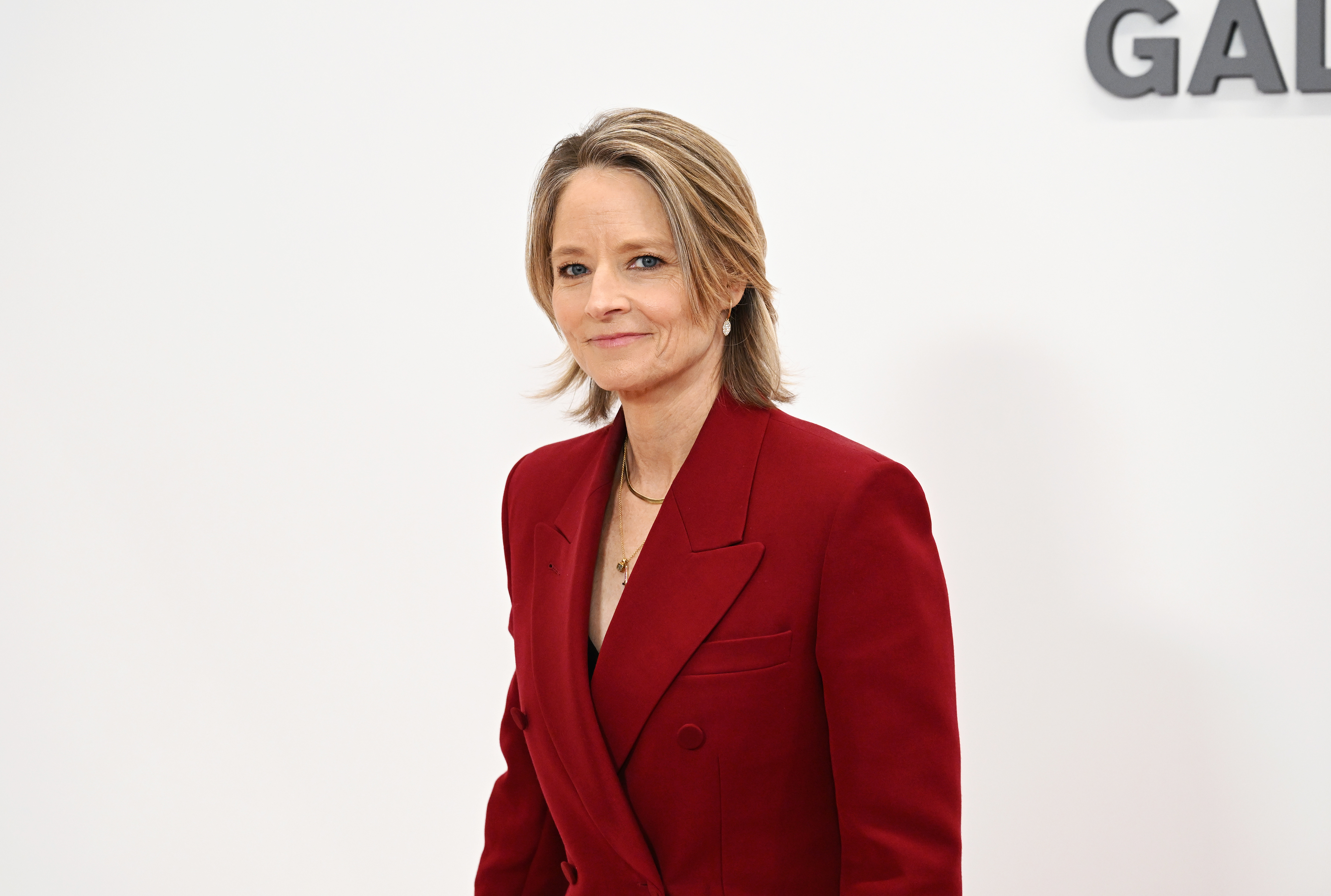 Jodie Foster stands against a plain backdrop wearing a stylish double-breasted blazer