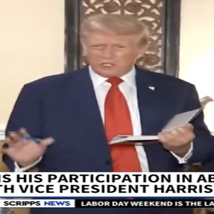 Trump speaks while holding a book, flanked by three people at news event in Falls Church, VA. News headline questions his ABC debate participation with Vice President Harris