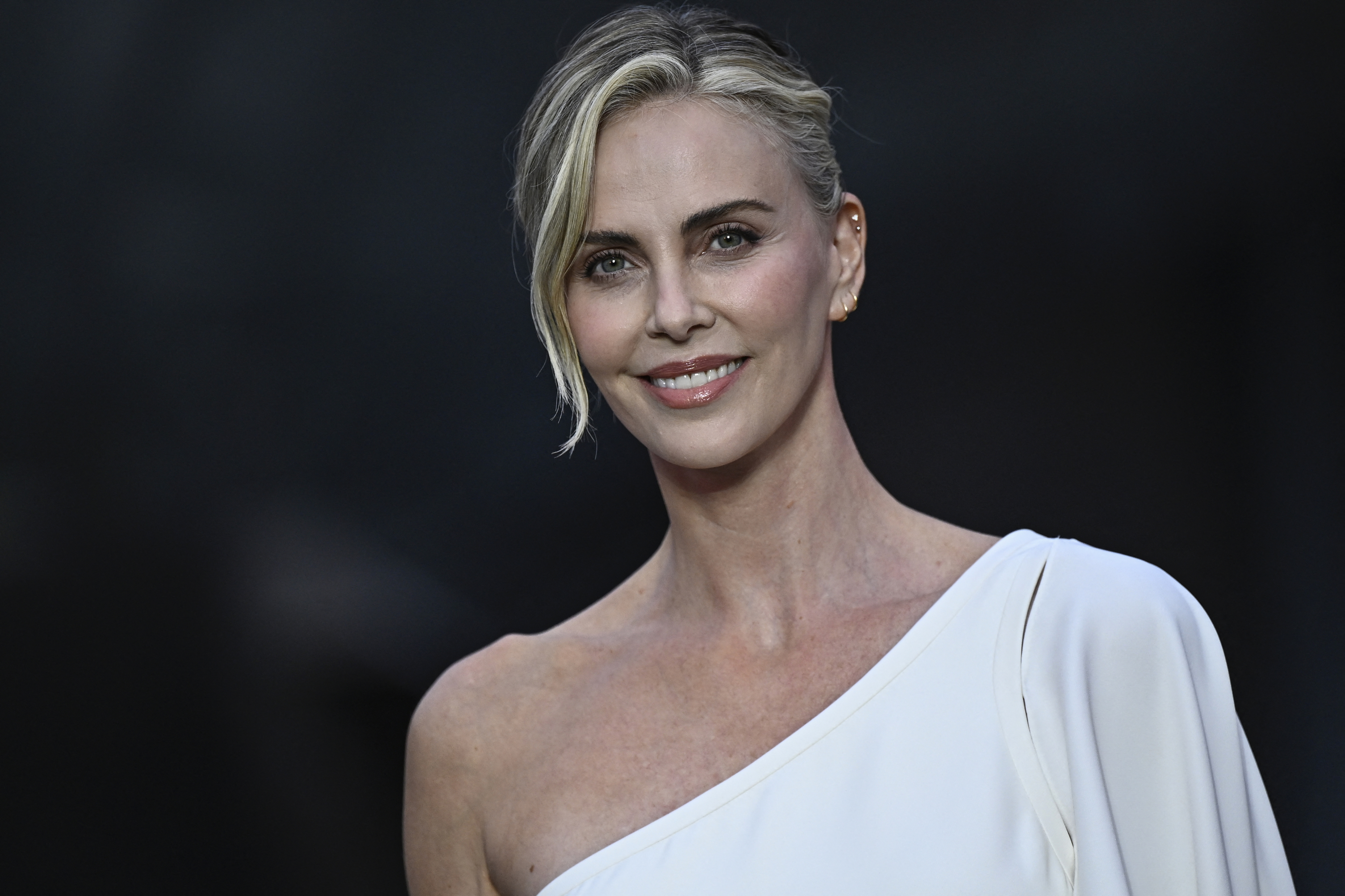 Charlize Theron smiles in an elegant one-shoulder dress