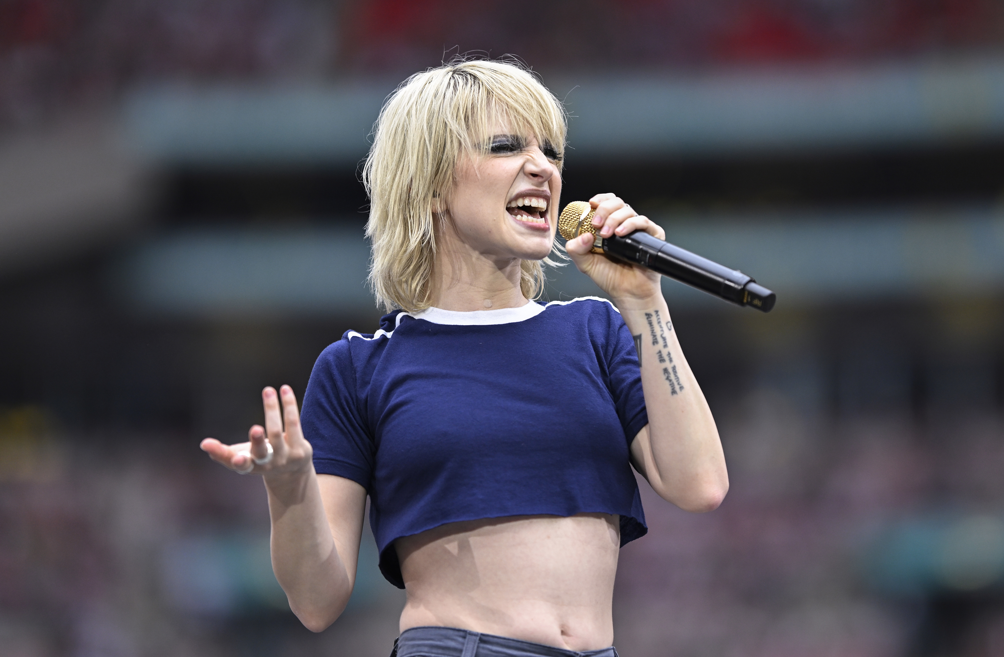 Hayley Williams singing passionately on stage, wearing a blue crop top and holding a microphone