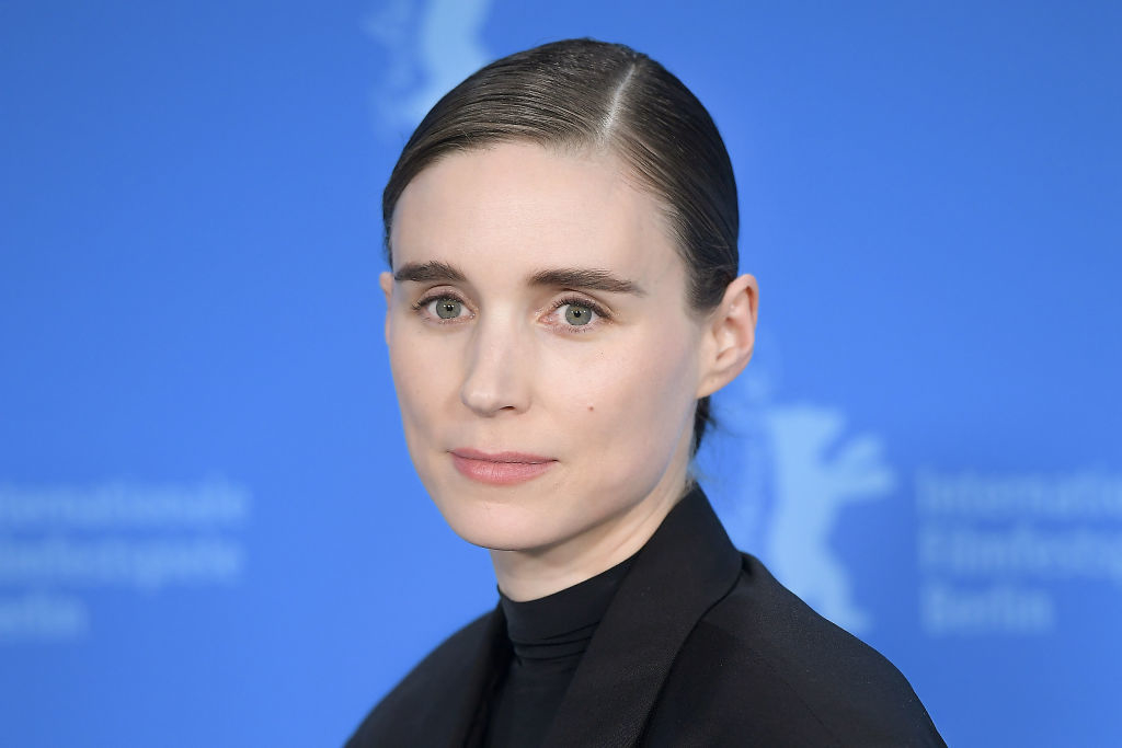 Rooney Mara attends a press event with her hair slicked back, wearing a black high-neck top and black blazer