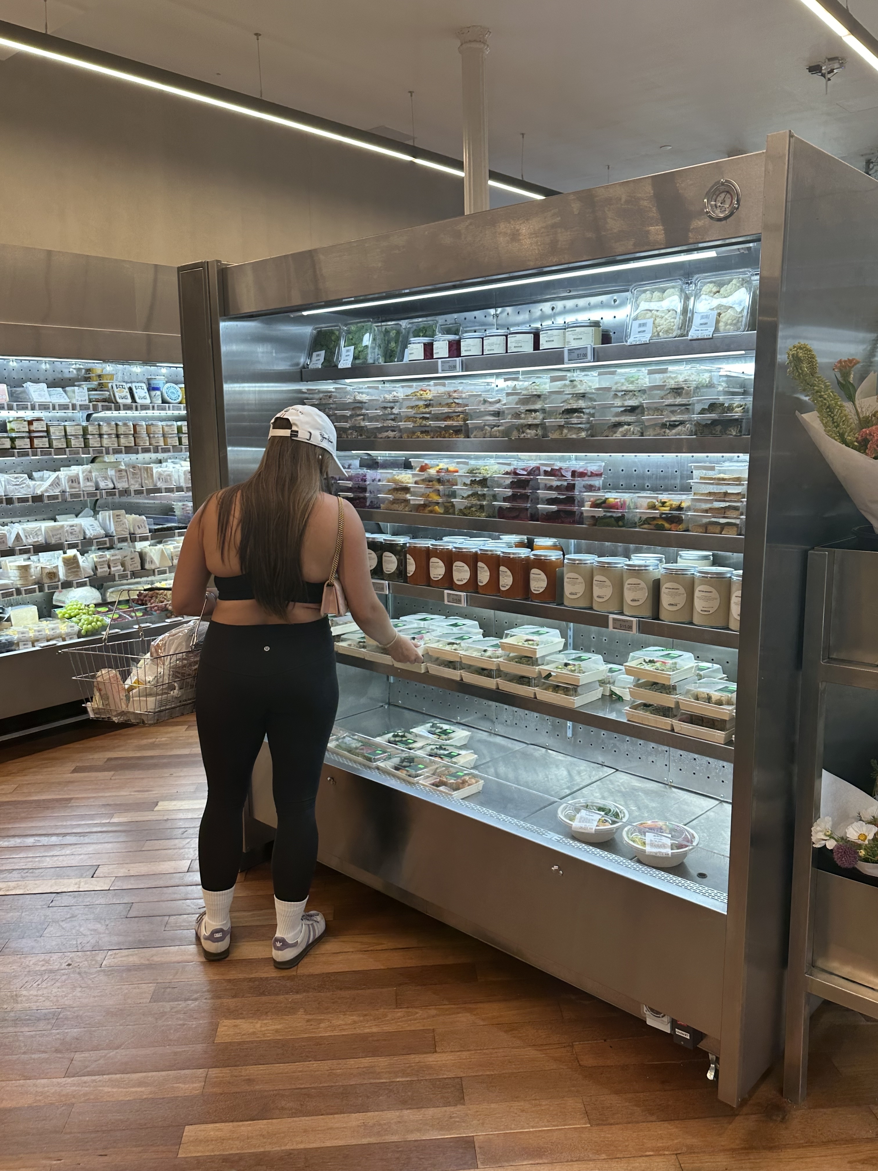 Person in athletic wear and cap browsing refrigerated food selections in a grocery store