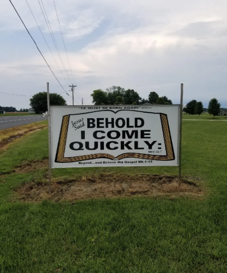 Roadside sign reads: "Jesus Said I Come Quickly. Rev 22:7. Repent… and Believe the Gospel Mk 1:15. Ye Must Be Born Again." It is set in a grassy field
