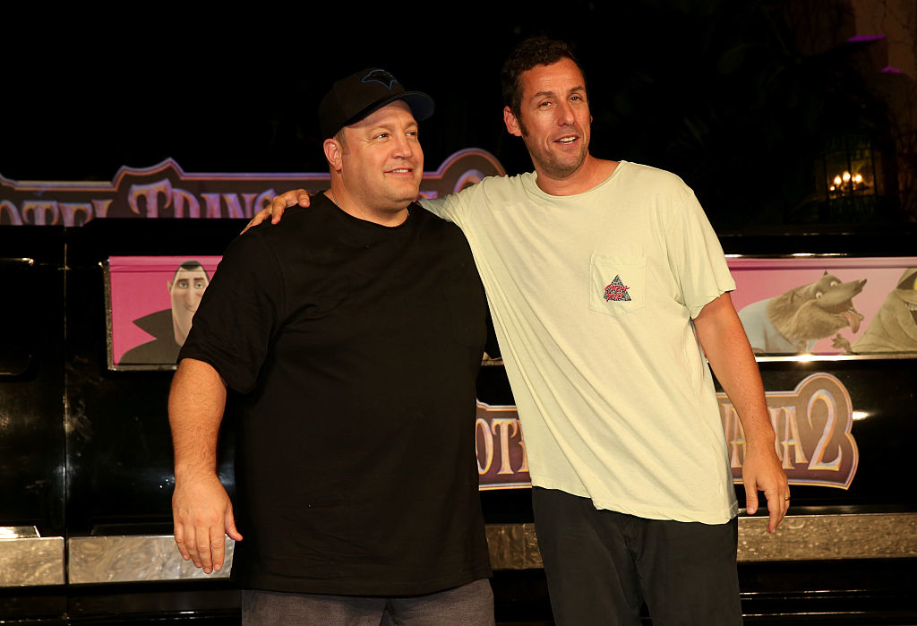 Kevin James in a black t-shirt and Adam Sandler in a light t-shirt stand together, smiling, at the "Hotel Transylvania 2" event