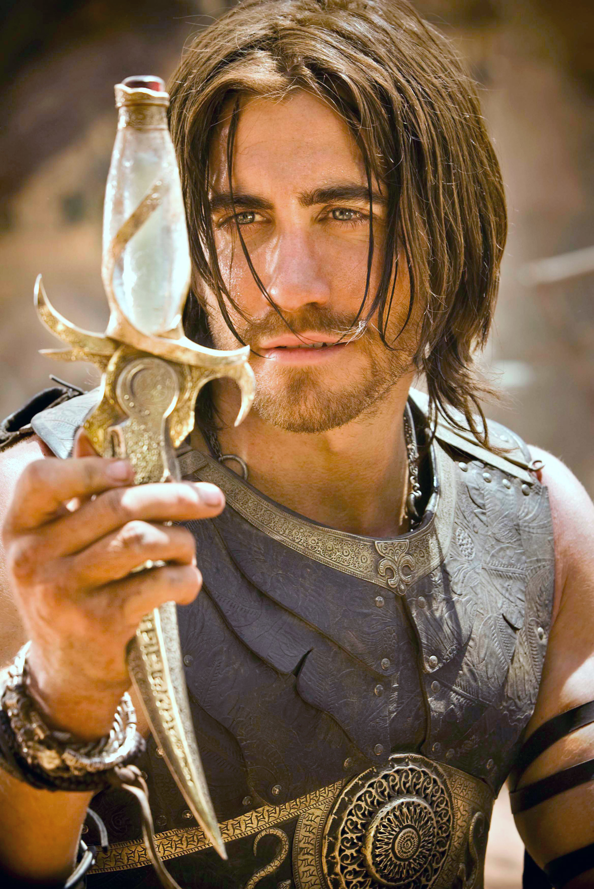 Jake Gyllenhaal, dressed in medieval armor, holds an ornate dagger while looking intently at it
