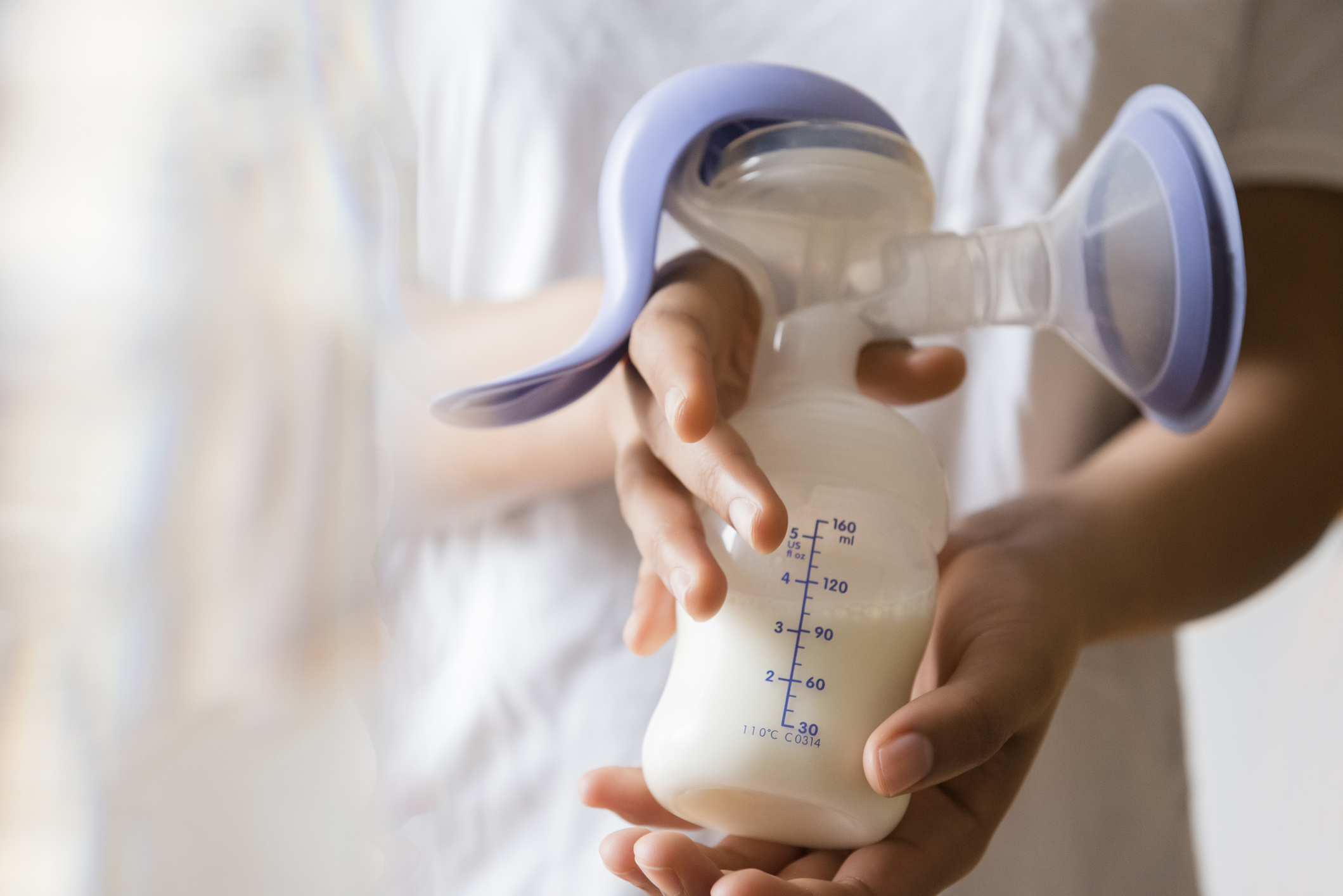 A person holding a manual breast pump with a milk bottle attached
