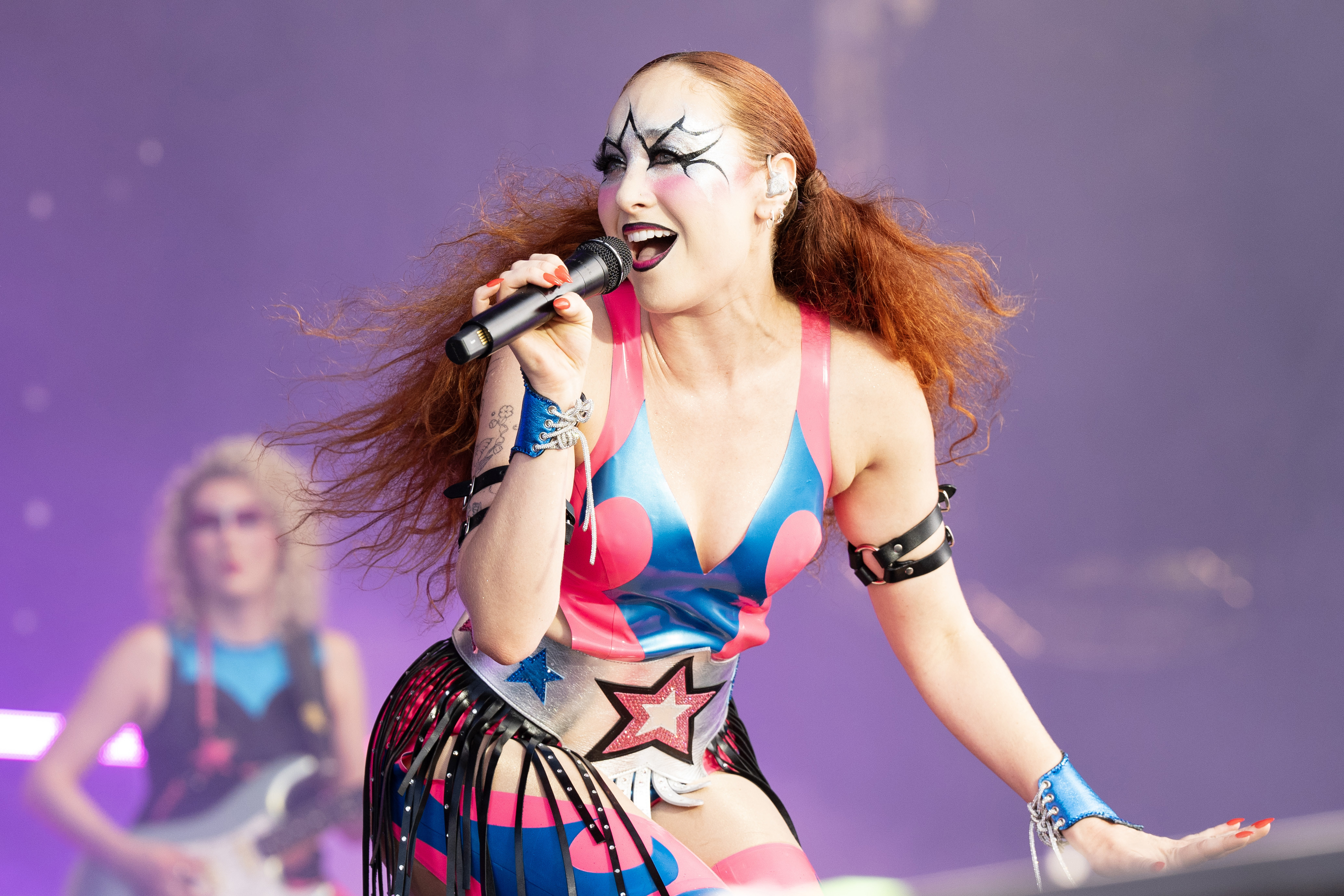 Chappell Roan performs on stage wearing a vibrant, star-themed outfit with bold face paint, reminiscent of 70's glam rock styles