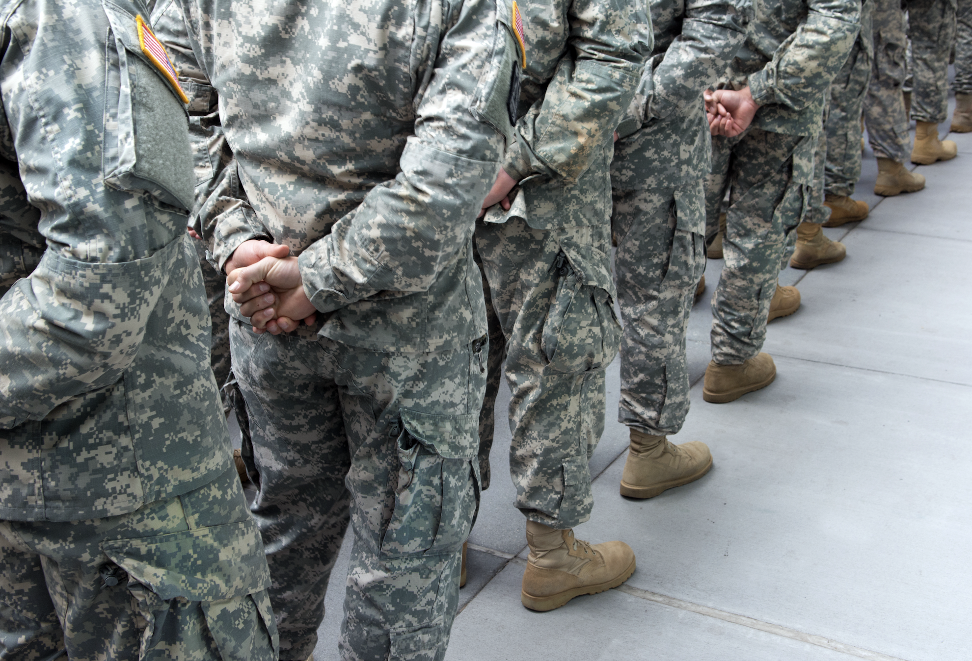 People in military uniforms standing in a row with their hands behind their backs. Faces are not visible