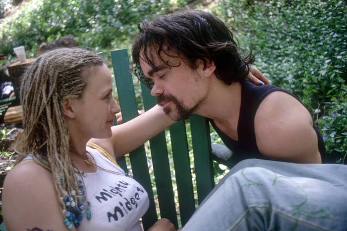 Patricia Arquette and Peter Dinklage sit on green chairs outdoors, gazing into each other's eyes. Arquette has braided hair and wears a tank top, Dinklage wears a sleeveless shirt