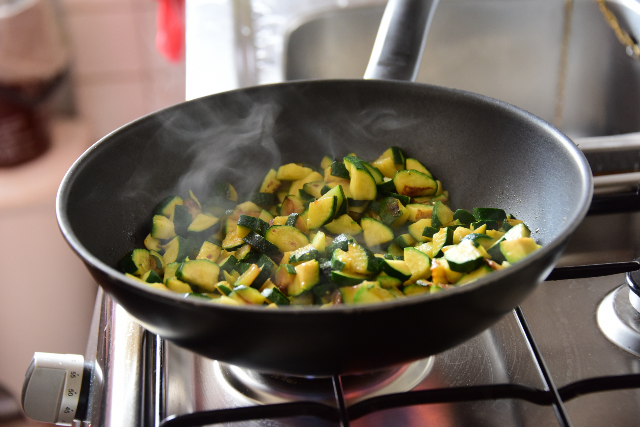 Sautéed zucchini pieces in a black frying pan on a stove, with steam rising, in a home kitchen setting