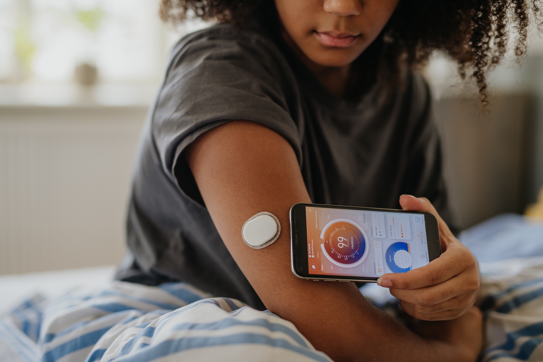 Person holding a smartphone displaying health data near a glucose monitoring patch on their arm, demonstrating diabetes management technology