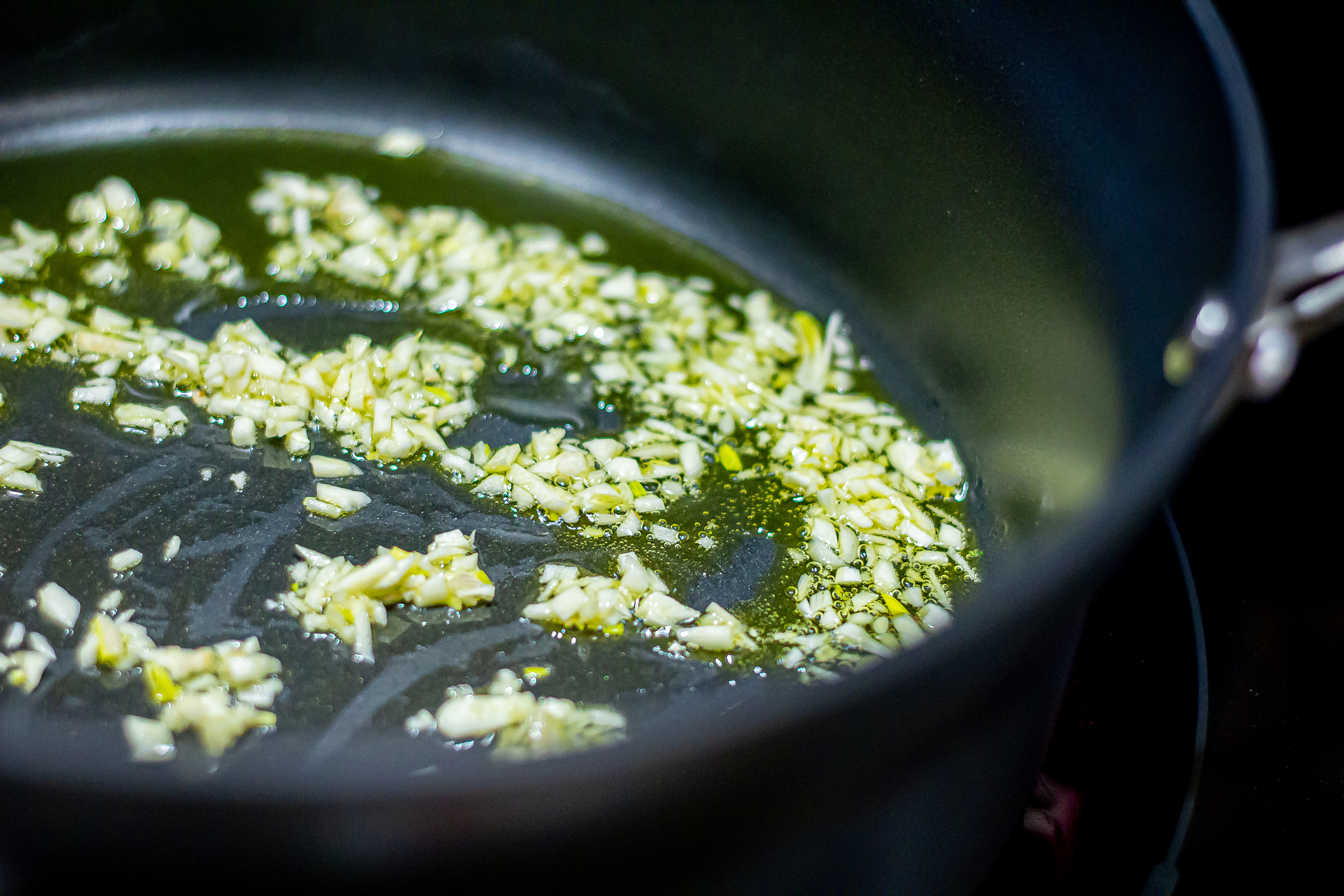 Chopped garlic being sautéed in a black frying pan with oil