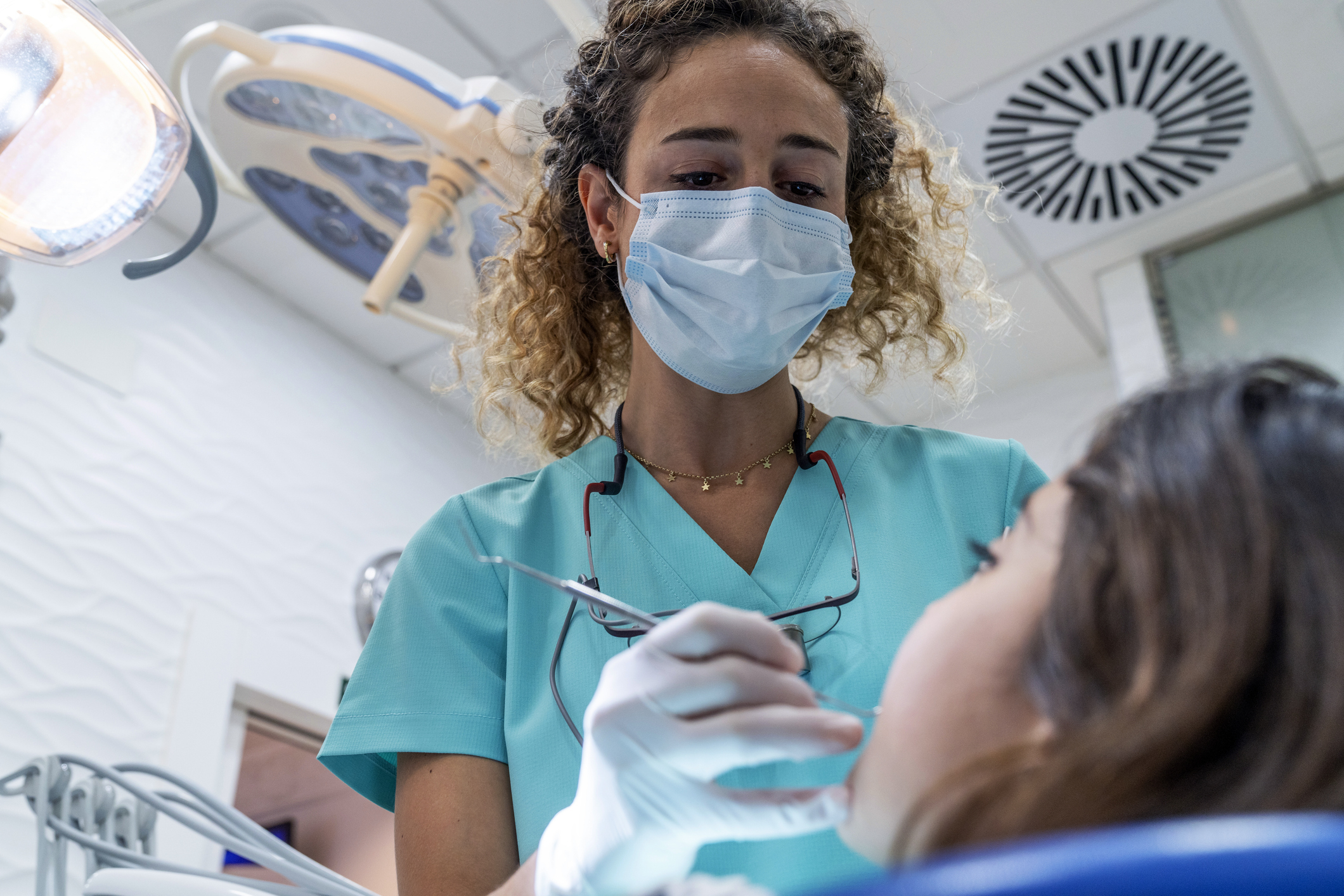 Dentist wearing a mask and gloves examines a patient&#x27;s teeth in a dental clinic