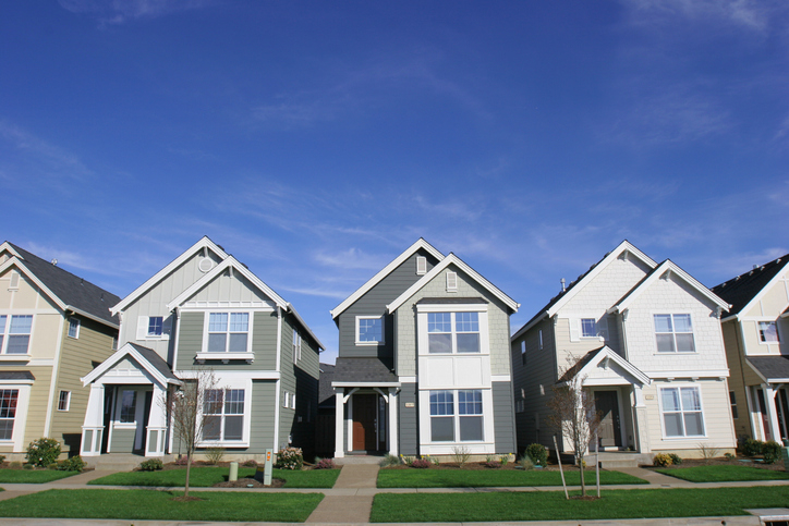 Three modern suburban homes with manicured lawns and clear blue skies above