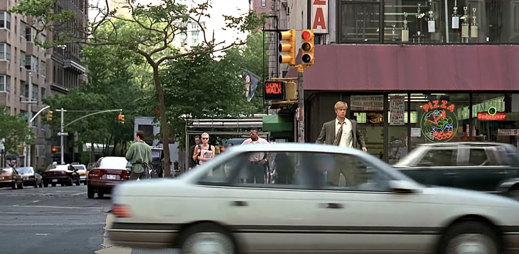 A busy city street scene with people walking on the sidewalk and cars moving in the foreground