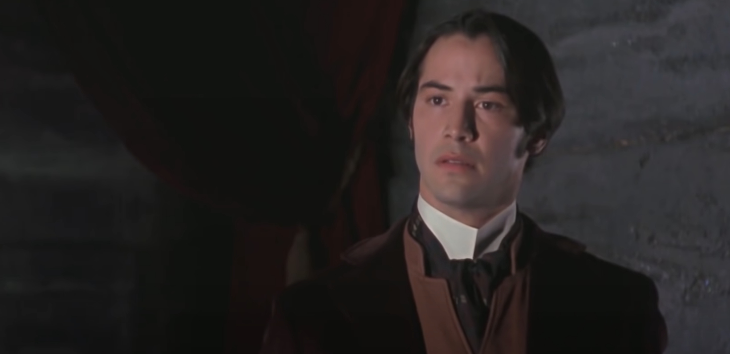 Keanu Reeves, in period attire, stands in a somber setting, appearing focused and introspective