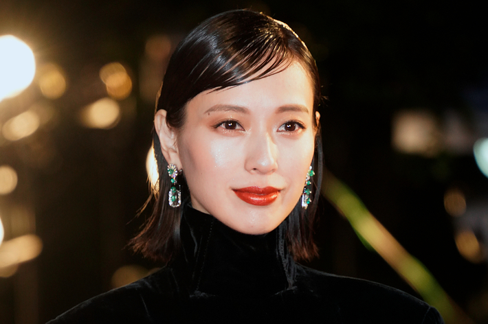 女性が豪華なドレスを身にまとい、レッドカーペットのような会場で微笑んでいる。