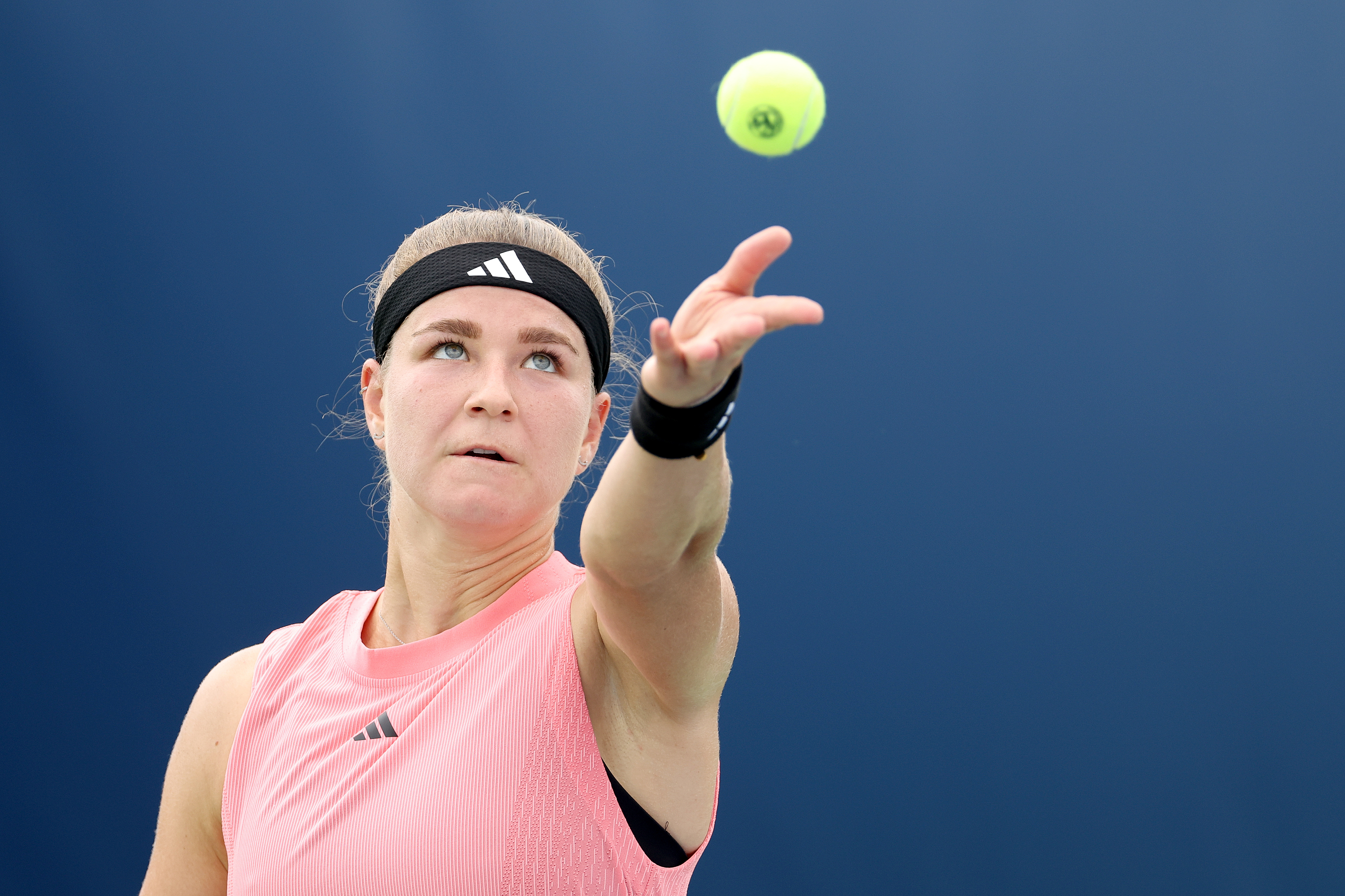Karolina Muchova serves during a tennis match wearing a sleeveless top and headband