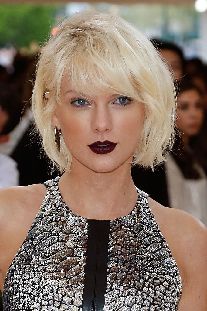Taylor Swift with a blonde bob hairstyle, wearing a sleeveless, patterned dress at a formal event