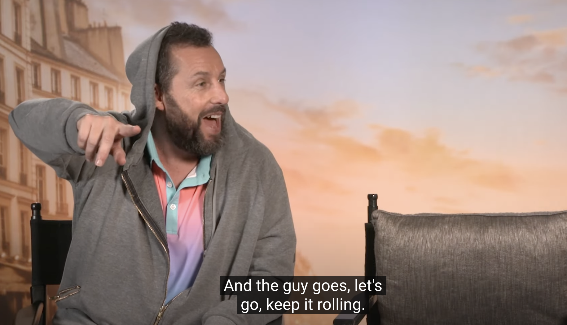 Adam Sandler, in casual attire with a hoodie, points and laughs during an interview. Caption: "And the guy goes, let's go, keep it rolling."