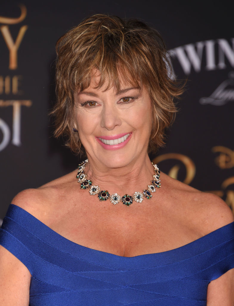 Debbie Reynolds smiles wearing a blue off-shoulder dress and a statement necklace at a red carpet event