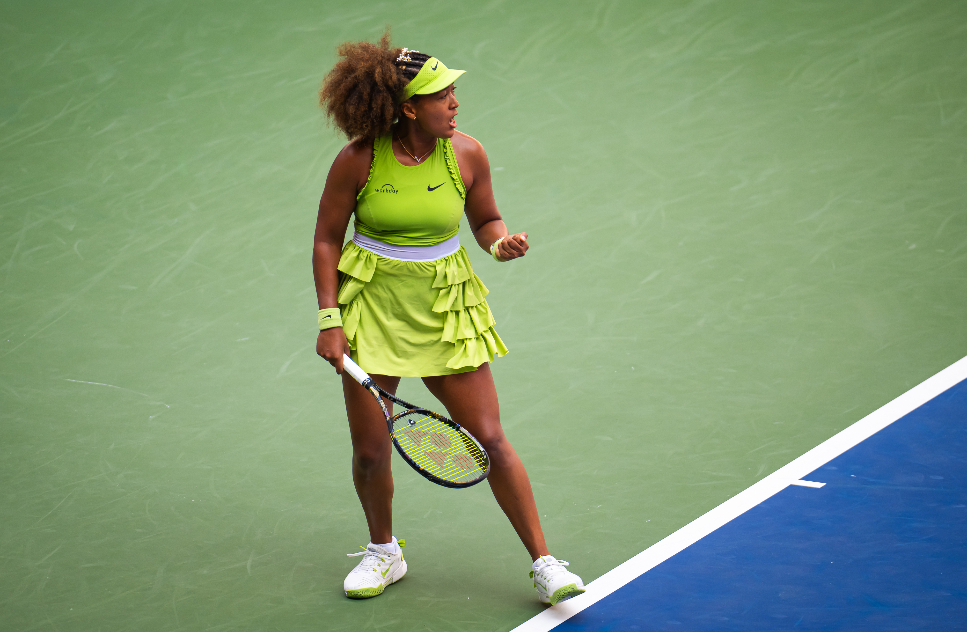 Naomi Osaka celebrates on the tennis court, wearing a sporty outfit and holding a racket, during a match