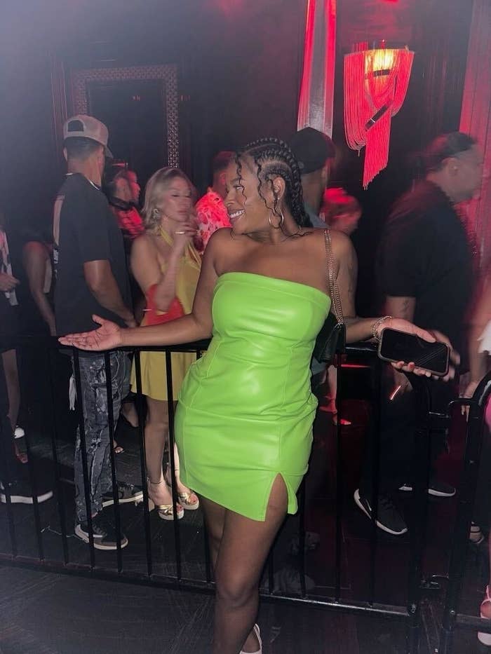 Rachel Parrish posing at a club with a crowd in the background. Rachel is wearing a short strapless green dress