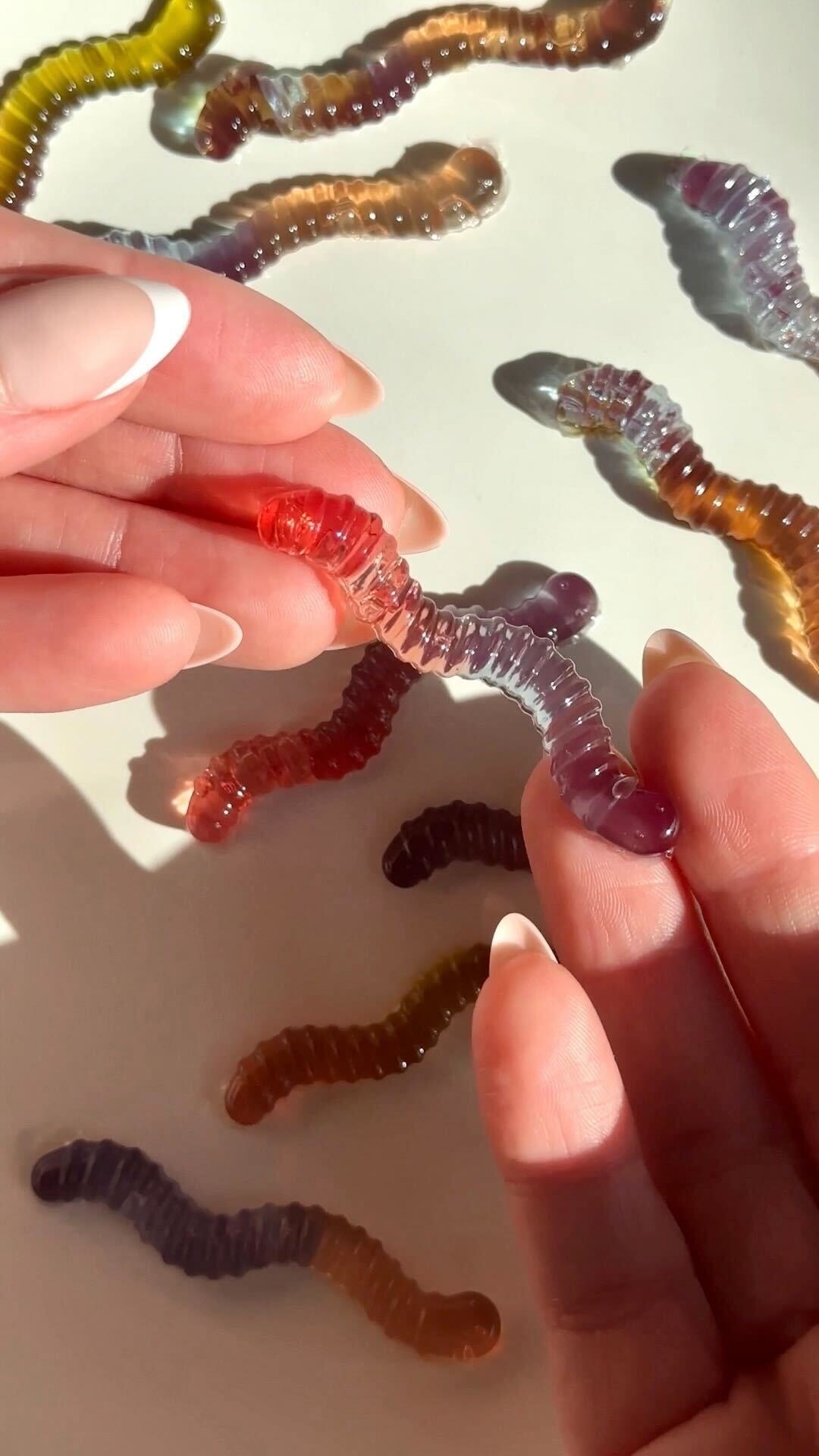Hands holding various colorful gummy worms on a white surface