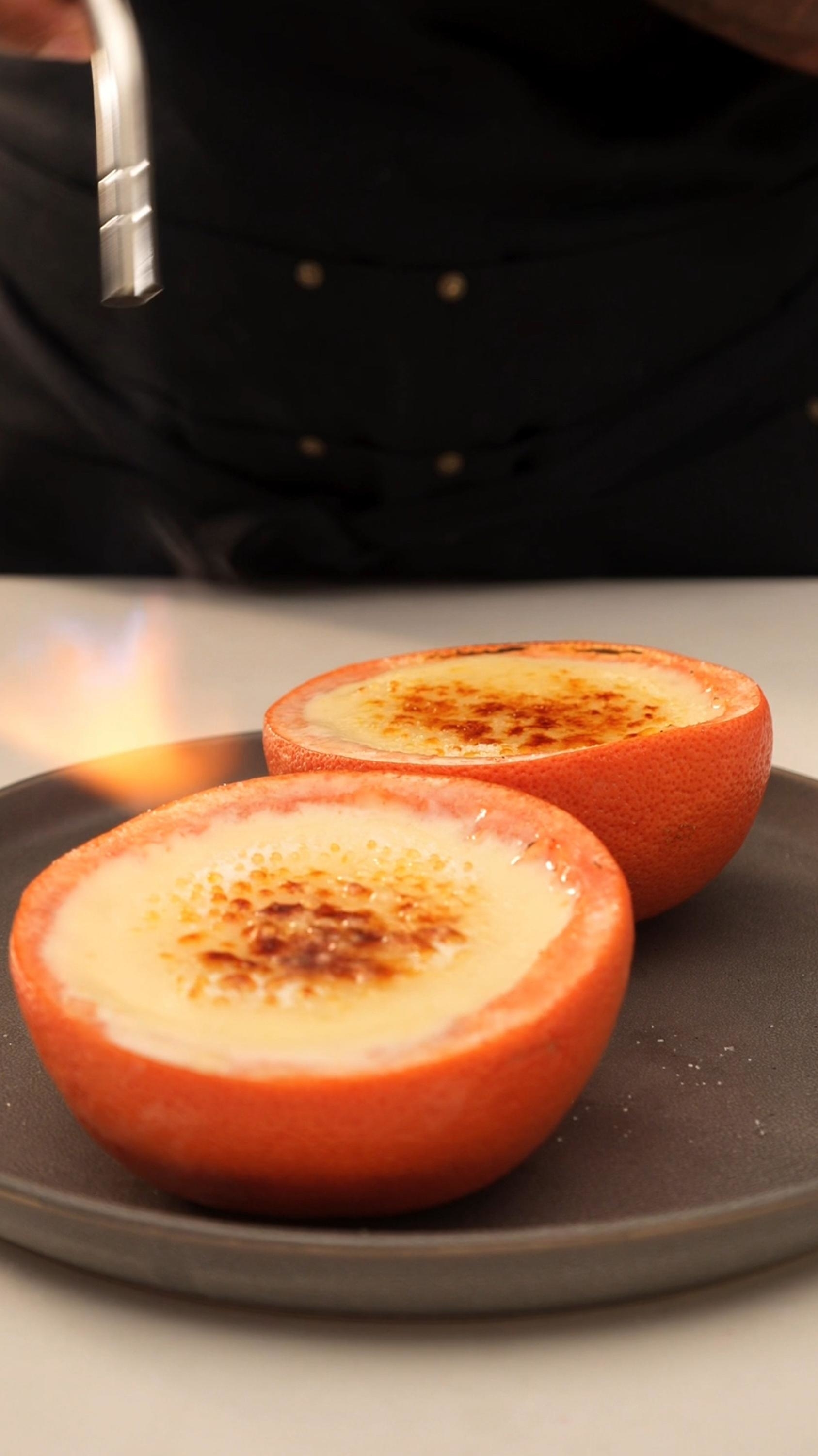 Two halved grapefruits being caramelized on top, resembling creme brulee, on a plate