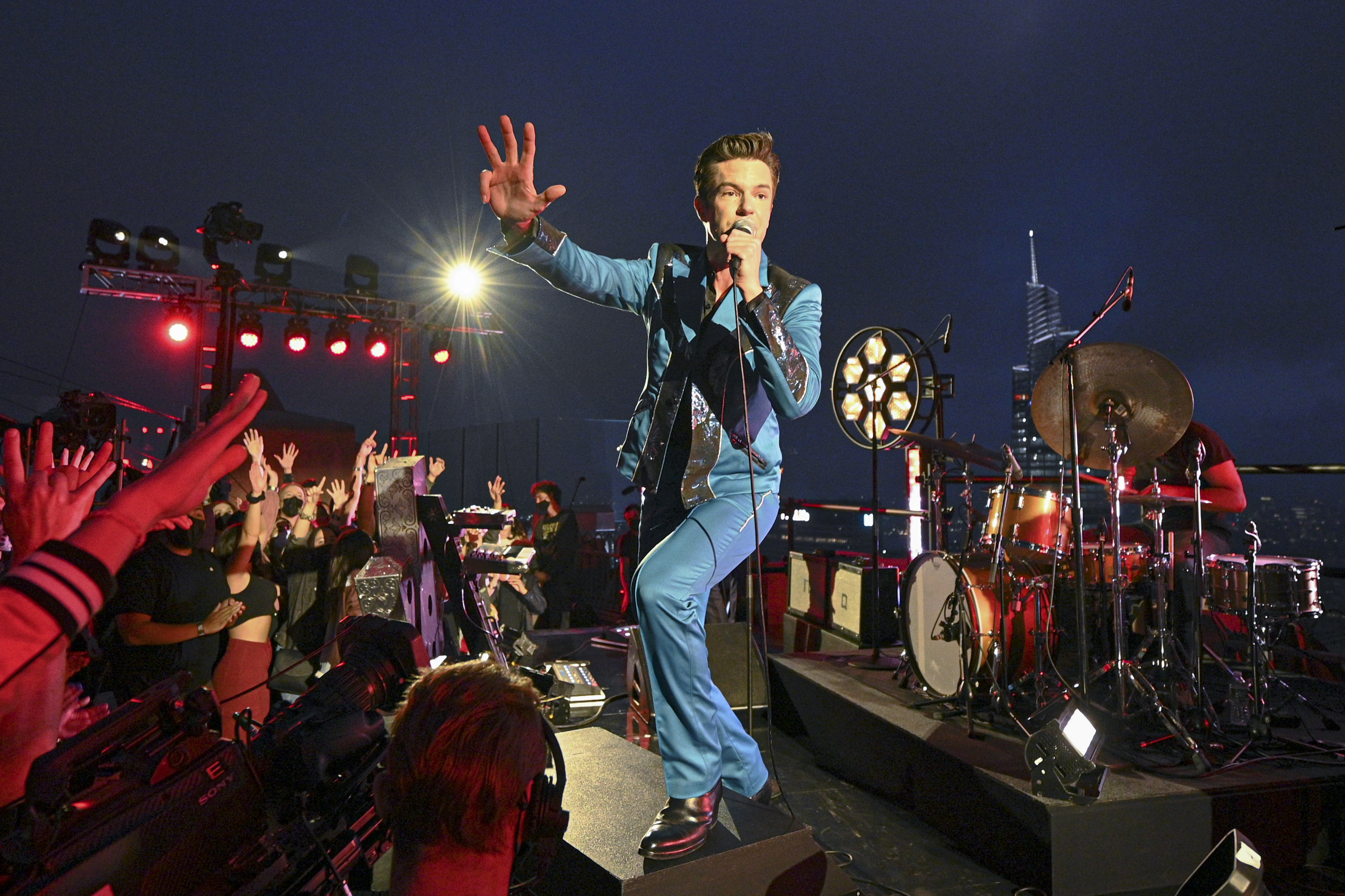 Brandon Flowers of The Killers performs on stage in front of a crowd in a blue suit