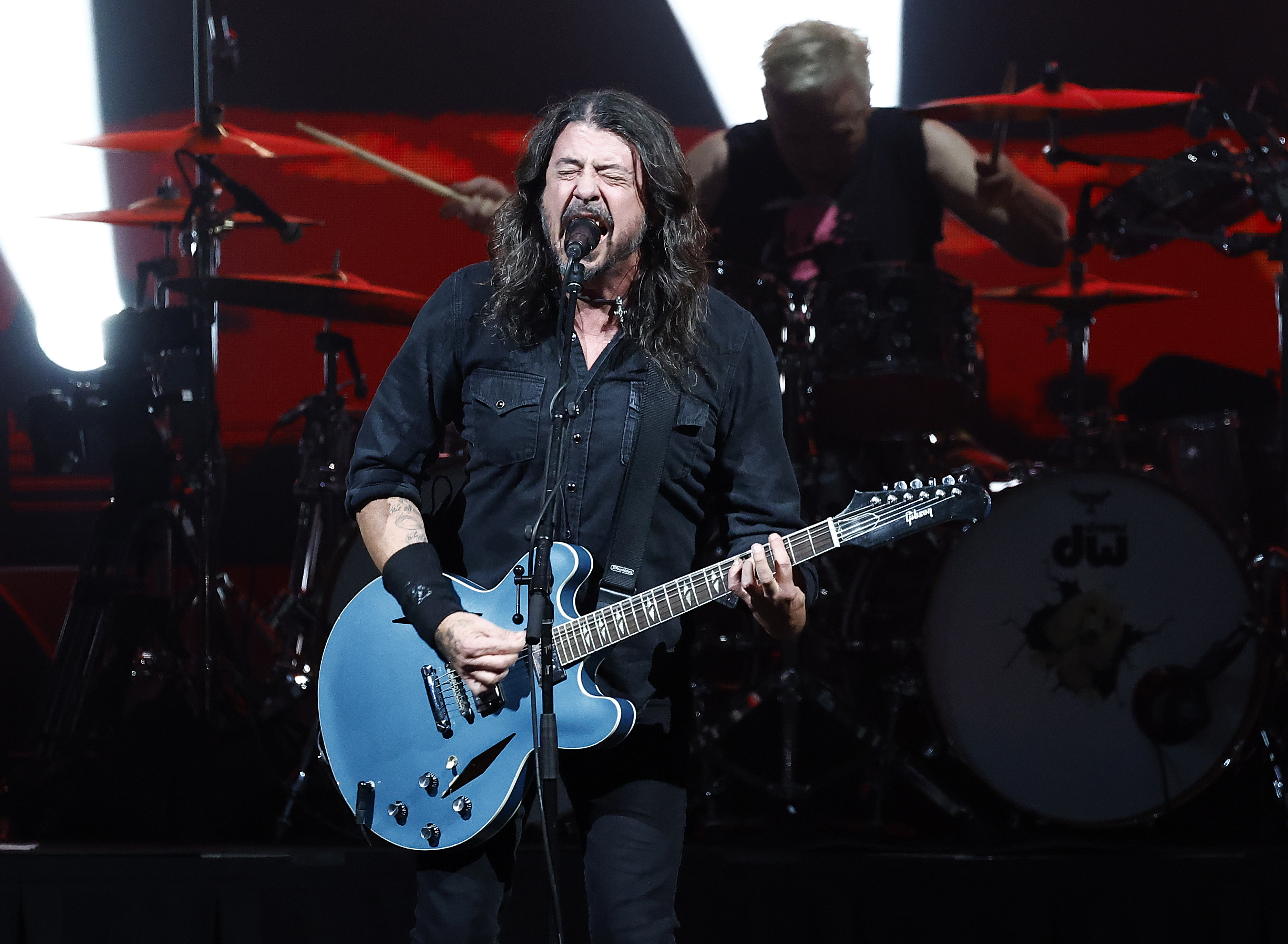 Dave Grohl performing live on stage with a guitar, drummer in the background