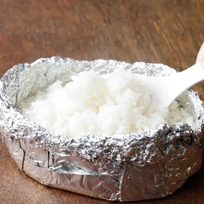 アルミホイルに包まれたご飯をヘラでよそう手。