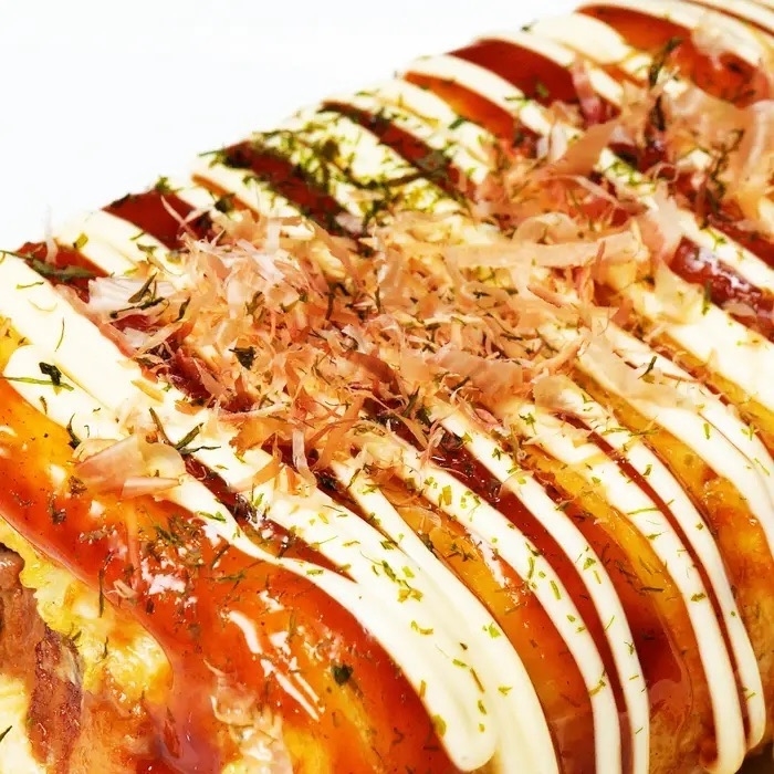 お好み焼きの接写画像。上にはかつお節、マヨネーズ、ソースがかかっている。